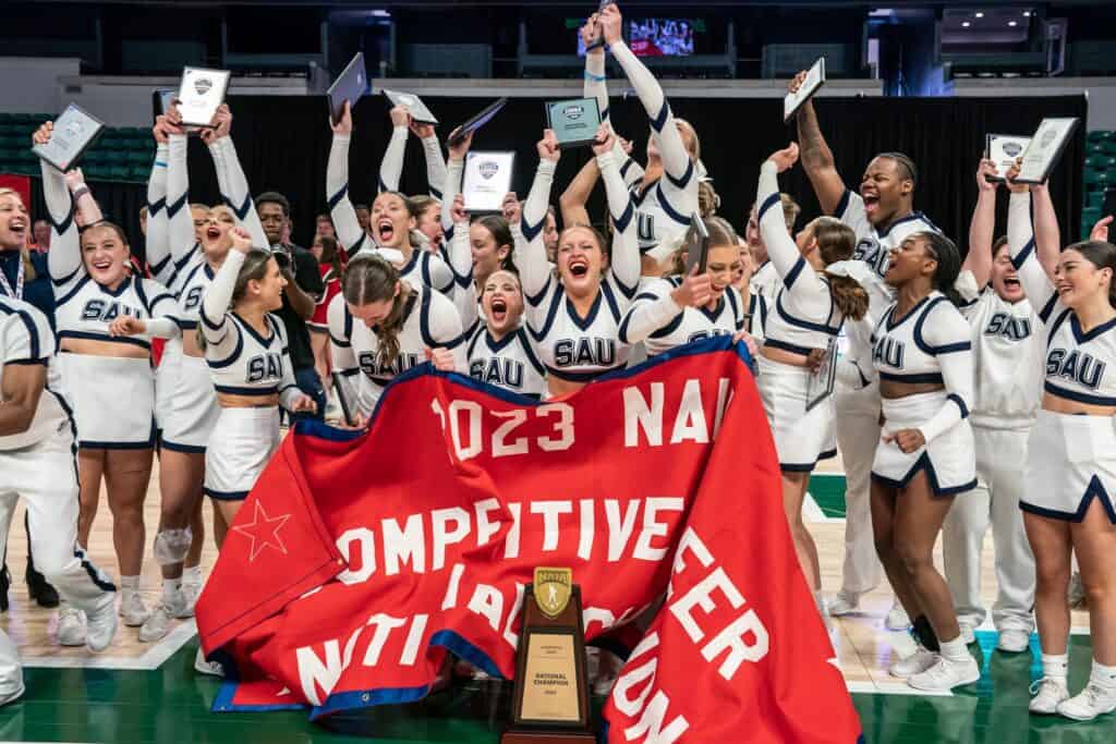 St. Ambrose Cheer team lifts up their banner and awards after winning a national championship. (Courtesy of saubees.com)