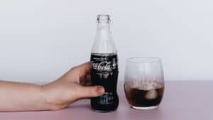 A person holding a bottle of coke next to a glass.