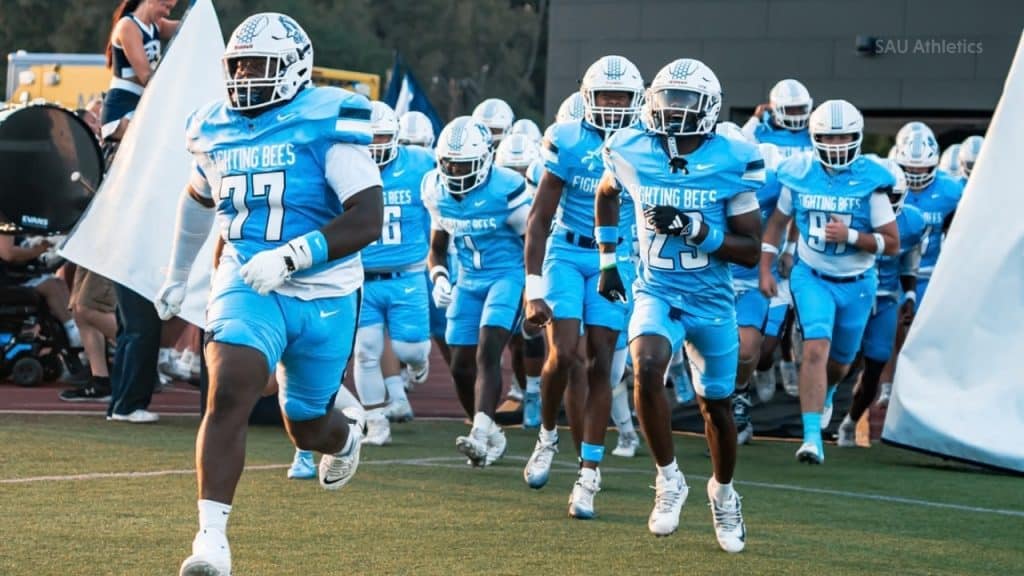 SAU football team in blue uniforms running onto the field for a game.