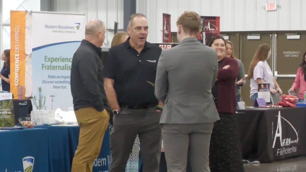 People networking at a career expo with booths and banners in the background.