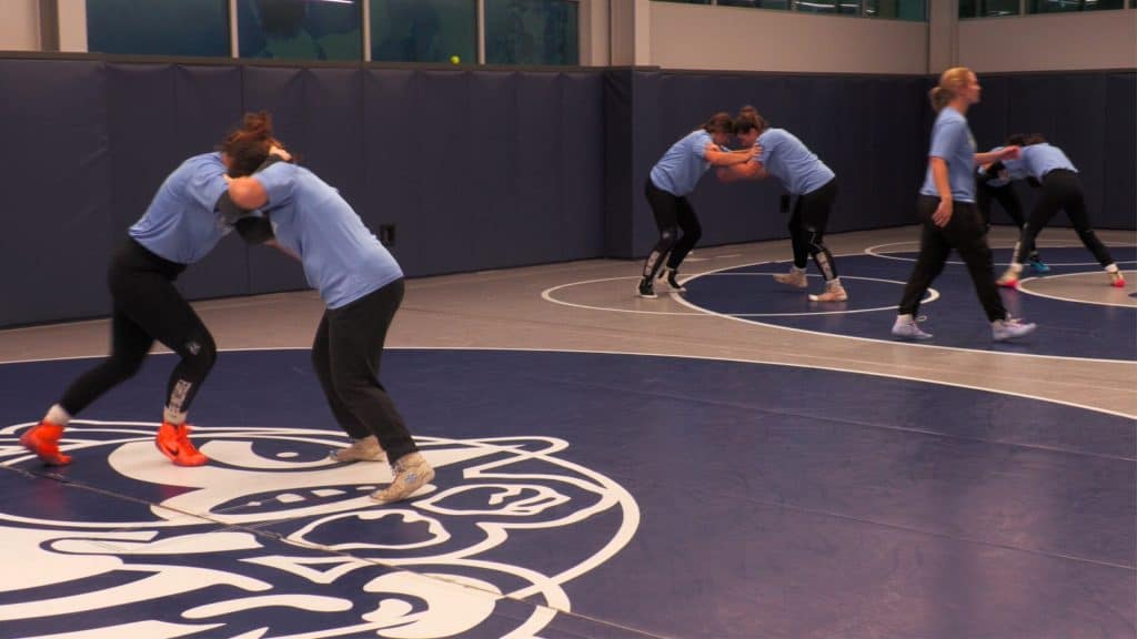 Women wrestlers practicing in a training facility with a blue mat and high hopes.