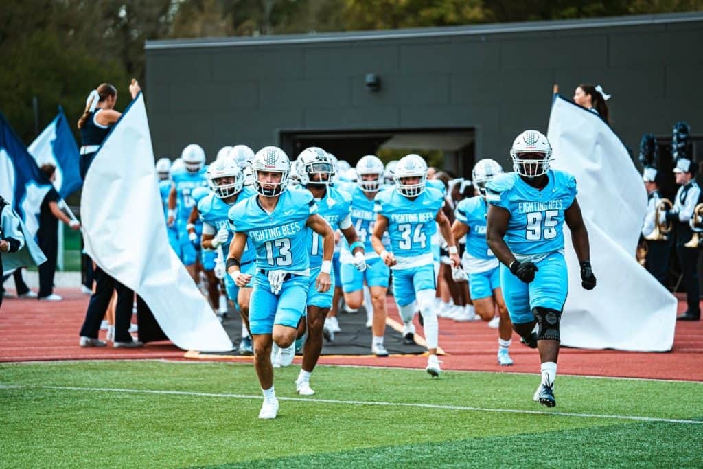 Fighting Bee football team entering the field with flags during homecoming event.