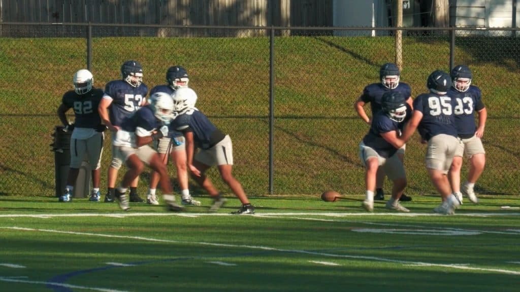 Youth football players practicing on the field during daytime.