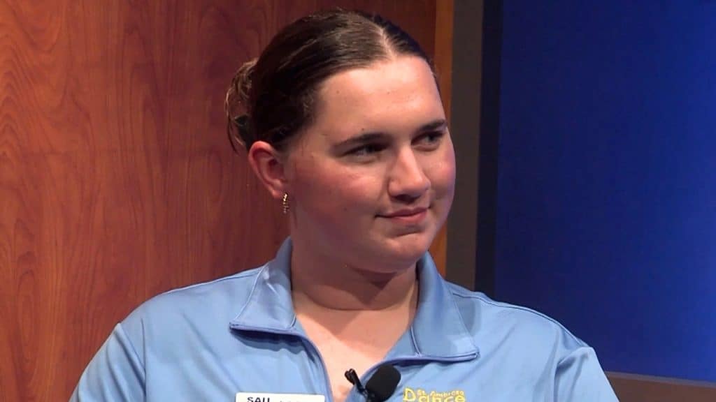 Young woman in blue uniform with SAU logo, smiling in a professional setting.