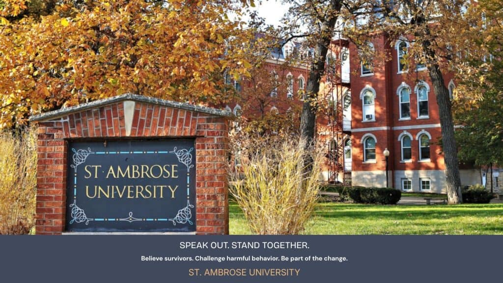 St. Ambrose University campus sign with brick building and autumn trees.